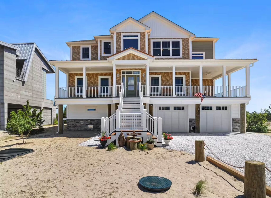 A beach house featuring a spacious deck and stairs leading to the sandy shore.